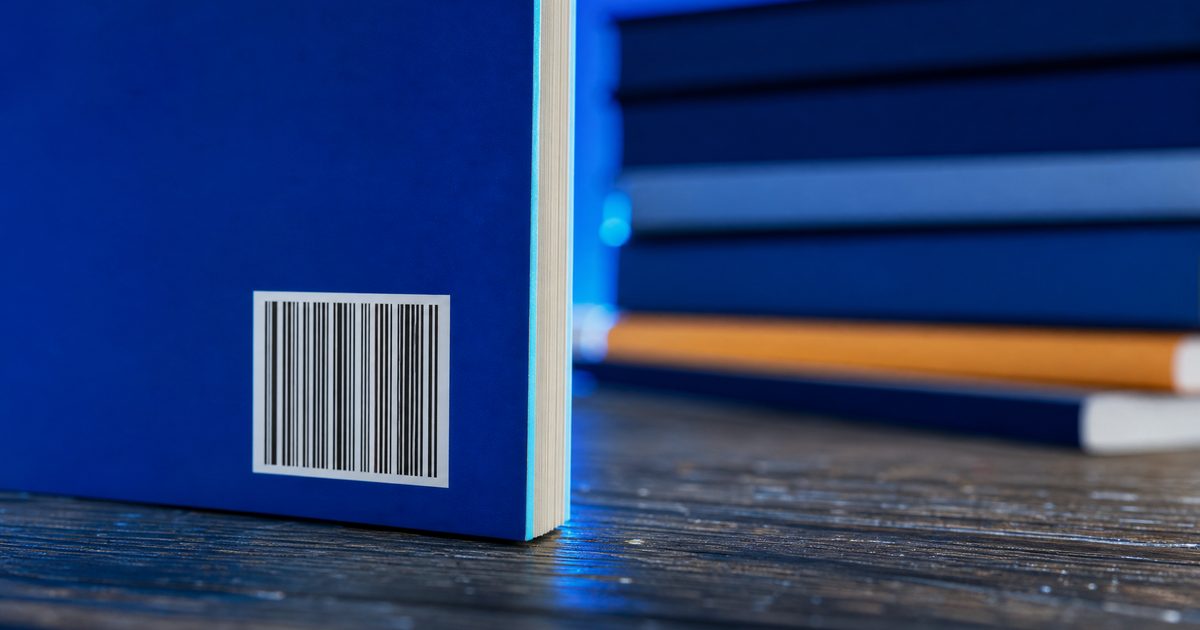 Close-up of the back cover of a paperback with its ISBN barcode, a stack of books blurred in the background